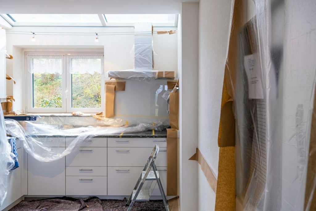 A kitchen undergoing construction with cabinets and countertops covered in protective plastic and brown paper.