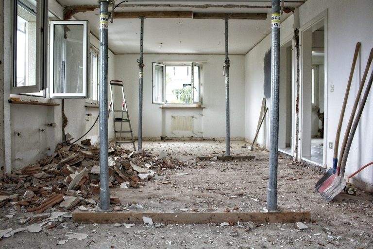 A room undergoing major structural renovation with metal support poles and construction debris.